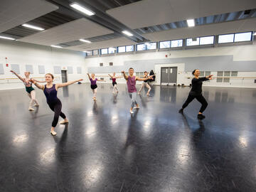 A large group dances in a ballet studio