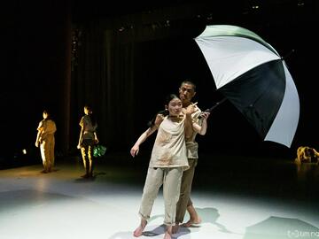 A shot of a stage production of two dancers holding an umbrella