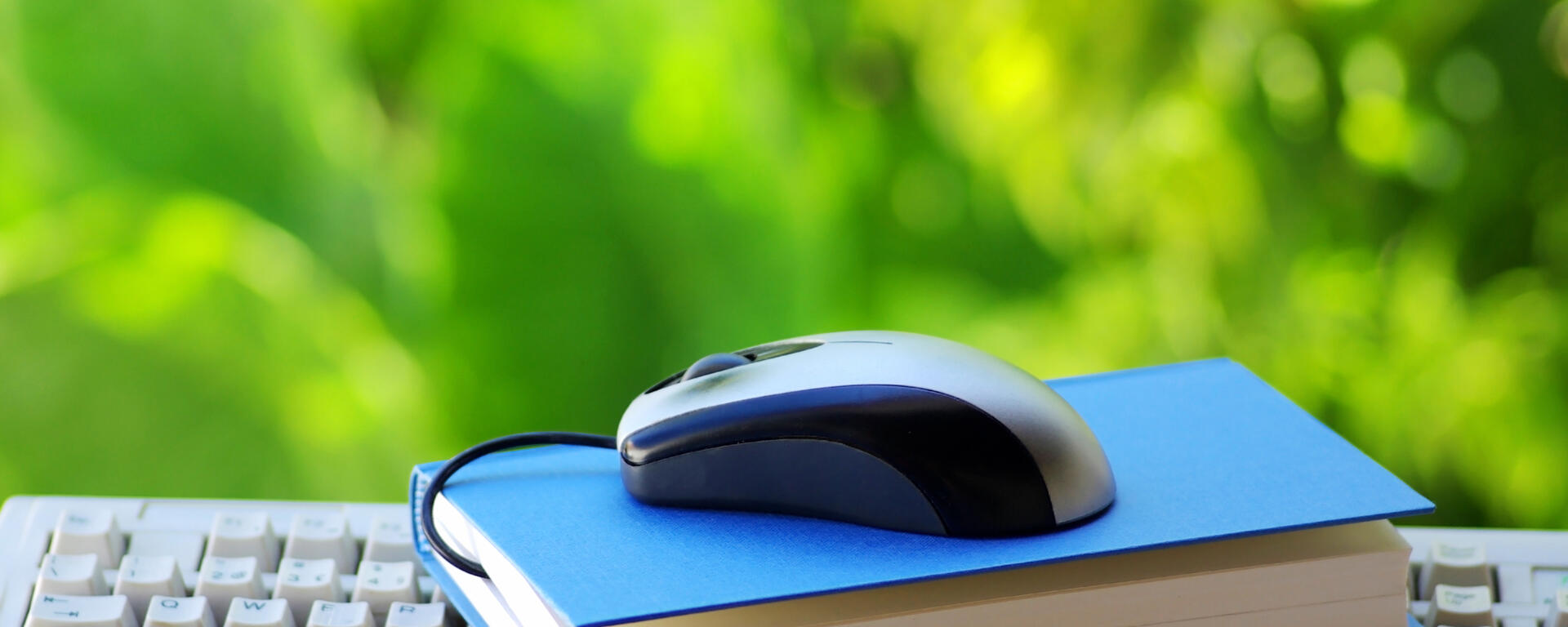 a keyboard with a blue book on top of it. A computr mouse is on top of the blue book